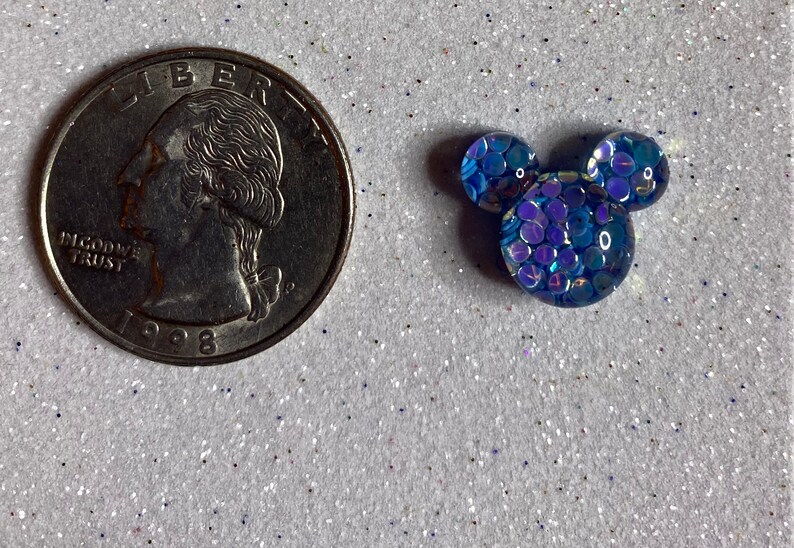 Op de afbeelding: Een blauwe, iriserende Mickey Mouse-kopbedel van hars. De bedel is ongeveer zo groot als een Nederlandse 2 euro munt.
