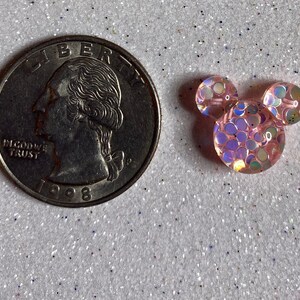 Op de afbeelding: Een roze en iriserende glitter Mickey Mouse-kop charme. De charme is ongeveer de grootte van een Amerikaanse kwart.