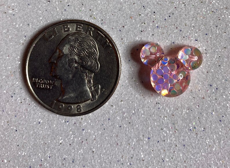 Op de afbeelding: Een roze en iriserende glitter Mickey Mouse-kop charme. De charme is ongeveer de grootte van een Amerikaanse kwart.