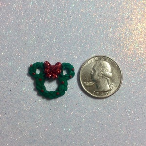 May include: A green Christmas wreath with a red bow and red berries, next to a US quarter for size comparison.