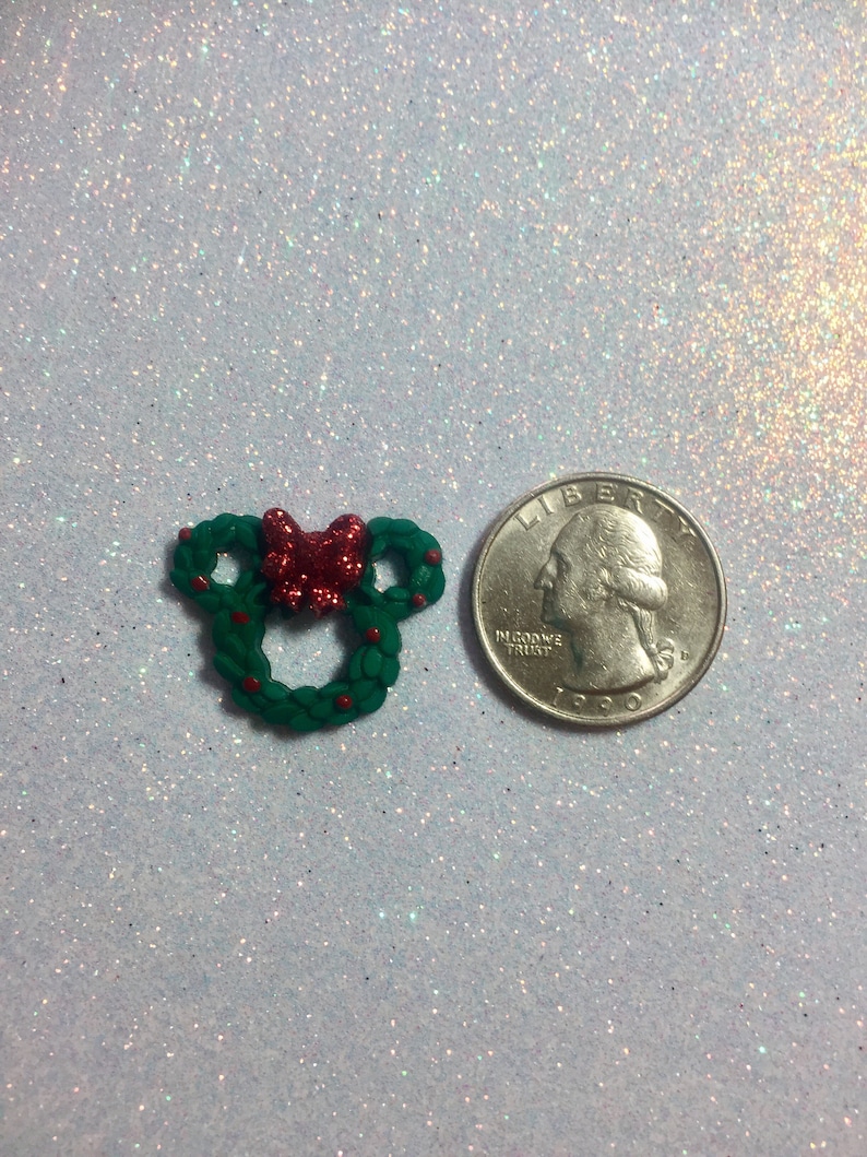 May include: A green Christmas wreath with a red bow and red berries, next to a US quarter for size comparison.