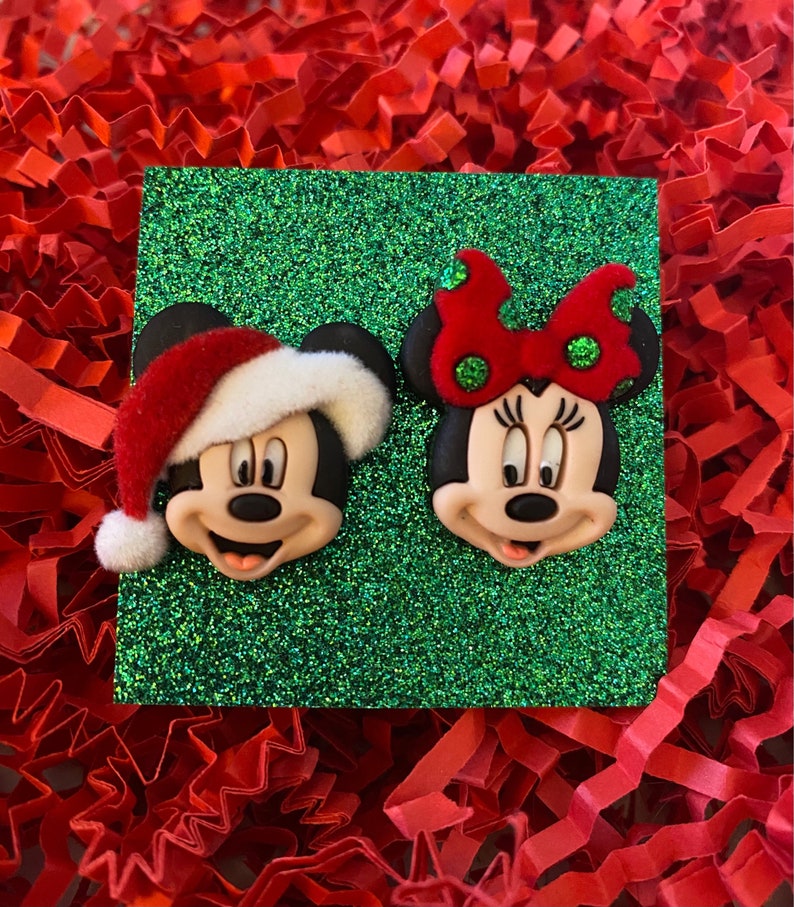 May include: A pair of Christmas-themed Mickey Mouse and Minnie Mouse earrings. Mickey is wearing a red Santa hat and Minnie has a red bow with white polka dots.
