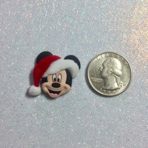 May include: A small, red and white Christmas-themed Mickey Mouse figurine with a Santa hat. The figurine is next to a US quarter for size comparison.