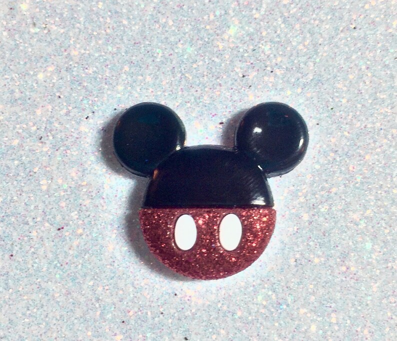 May include: A red and black glitter Mickey Mouse head with white eyes.