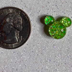 Op de afbeelding: Een groene, iriserende, met glitter gevulde Mickey Mouse-kop charme. De charme is ongeveer zo groot als een Nederlandse 2 euro munt.