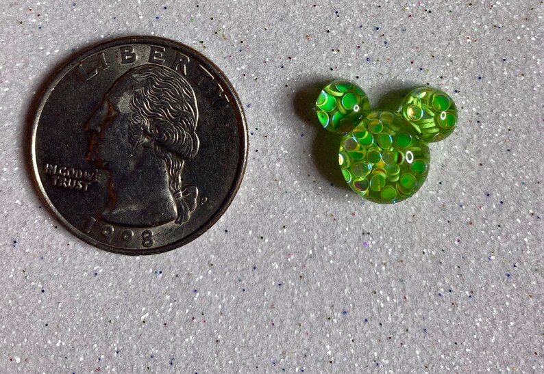 Op de afbeelding: Een groene, iriserende, met glitter gevulde Mickey Mouse-kop charme. De charme is ongeveer zo groot als een Nederlandse 2 euro munt.