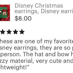 May include: A pair of Christmas-themed Disney earrings featuring Mickey Mouse and Minnie Mouse. Mickey is wearing a Santa hat and Minnie is wearing a red bow. The earrings are made of a fuzzy material.