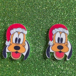 May include: A pair of Christmas-themed earrings featuring a cartoon dog wearing a Santa hat. The dog has brown fur, a black nose, and white eyes. The earrings are made of white plastic and have a shiny, glittery finish.