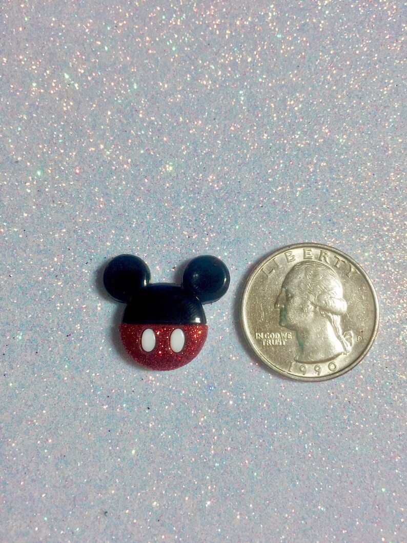 May include: A red, white, and black Mickey Mouse character charm with glitter. The charm is about the size of a US quarter.