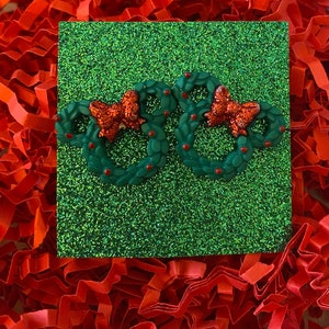 May include: Two green Christmas wreaths with red bows and red berries on a green glitter background.