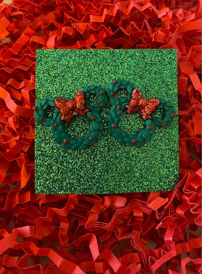 May include: Two green Christmas wreaths with red bows and red berries on a green glitter background.
