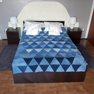 May include: A white headboard with a blue and white quilt on a bed. The bed has two white pillows with floral embroidery. There are two bedside tables with lamps on each side of the bed.