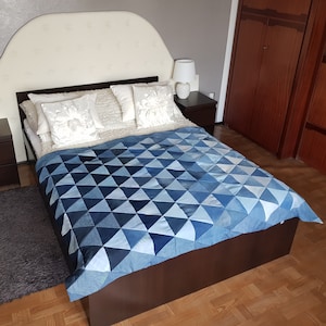 May include: A bed with a white headboard and a blue denim quilt. The bed has two nightstands with lamps on them. The room has a wooden floor.