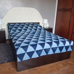 May include: A white headboard with a tufted design, a blue and white geometric patterned bedspread, and two white bedside lamps with white shades.