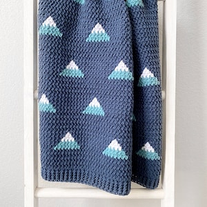 May include: A blue crocheted baby blanket with a white and teal mountain pattern.