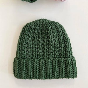 May include: A green knitted beanie hat with a folded brim. The hat is made with a textured stitch pattern.
