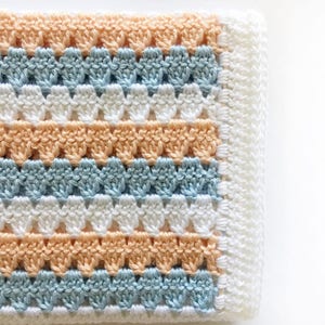 May include: A crocheted baby blanket with a striped pattern in peach, light blue and white.