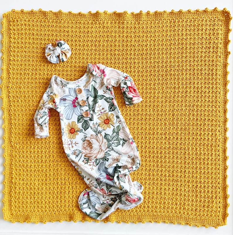 Pu&ograve; includere: Una copertina per neonati in crochet color giallo senape con un vestito annodato a stampa floreale e un fiocco per capelli in cima.