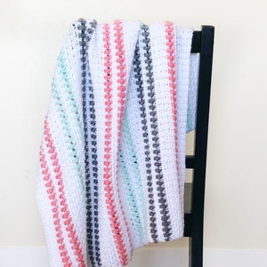 May include: A white crocheted blanket with stripes of pink, gray, and mint green. The blanket is draped over a black chair.