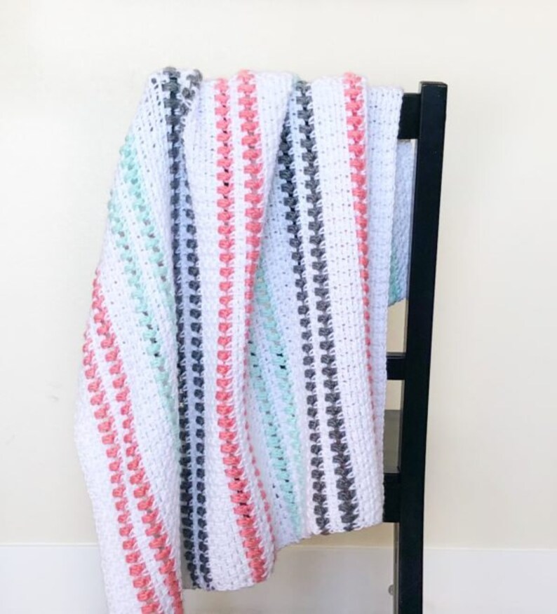 May include: A white crocheted blanket with stripes of pink, gray, and mint green. The blanket is draped over a black chair.