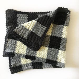 Peut inclure: Une couverture en crochet noire, grise et crème avec un motif à carreaux.