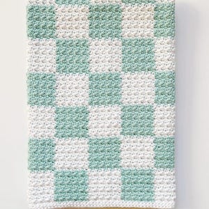 Op de afbeelding: Een gehaakt babydekentje met een geruit patroon in wit en lichtgroen.