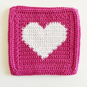 May include: A pink crocheted square with a white crocheted heart in the center.