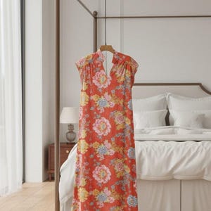 Könnte beinhalten: Rotes Kleid mit Blumenmuster, hohem Ausschnitt und kurzen Ärmeln. Das Kleid wird auf einem goldenen Ständer in einem Schlafzimmer präsentiert. Das Vanity Fair-Logo ist oben rechts sichtbar.