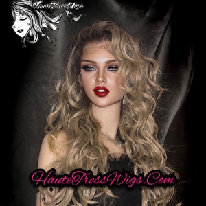 Puede incluir: Una mujer con el pelo largo, ondulado y rubio claro, lleva un vestido negro con lunares blancos y un estola de piel negra. Lleva lápiz labial rojo y tiene esmalte de uñas rojo. El texto "Haute Tress Wigs.Com" es visible en la imagen.