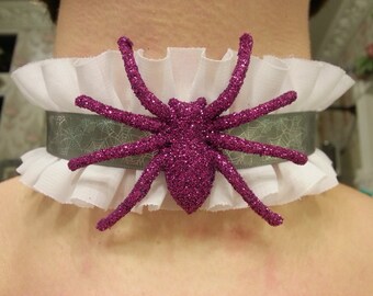 May include: A white ruffled choker with a sparkly pink spider charm. The spider has a glittery finish and is a popular Halloween accessory.