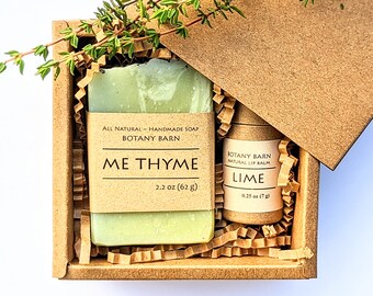 May include: A brown cardboard box containing a green bar of soap and a tube of lip balm. The soap is labelled "Me Thyme" and the lip balm is labelled "Lime". Both products are from Botany Barn.