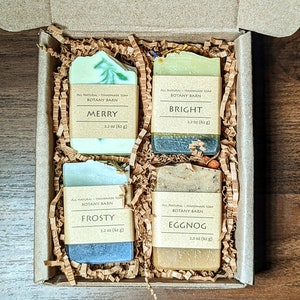 May include: A set of four handmade soap bars in a cardboard box with shredded paper. The soap bars are labelled "Merry", "Bright", "Frosty", and "Eggnog". Each bar is 62 grams.