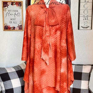 May include: A coral orange dress with a honeycomb pattern and a bow tie. The dress is on a mannequin and has a high-low hemline. The text "Luisa Love 30" is visible on the dress.