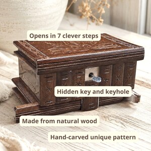 May include: A dark brown wooden puzzle box featuring hand-carved patterns on the lid and sides. The box includes a hidden key and keyhole mechanism, and the text on the image indicates it opens in 7 clever steps and is made from natural wood.