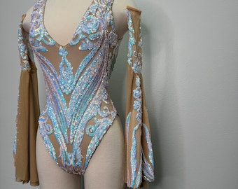 Könnte beinhalten: Ein nudefarbener Body mit schimmernden Pailletten in einem Blumenmuster. Der Body hat lange, durchsichtige Ärmel mit Glockenärmeln.