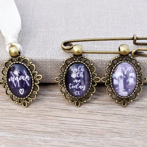 Könnte beinhalten: Drei bronzene Broschen mit ovalen Glaseinsätzen. Die erste Brosche hat den Text "mama" in weißen Buchstaben auf schwarzem Hintergrund. Die zweite Brosche hat den Text "Walk with me today" in weißen Buchstaben auf schwarzem Hintergrund. Die dritte Brosche hat ein Schwarzweißfoto einer Hochzeitsgesellschaft.