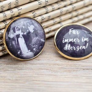 Könnte beinhalten: Zwei runde, goldgerahmte Glas-Foto-Anhänger. Ein Anhänger zeigt ein Schwarzweißfoto eines Brautpaares und zweier Gäste. Der andere Anhänger hat einen lila Hintergrund mit dem Text "Für immer im Herzen!" in Weiß.