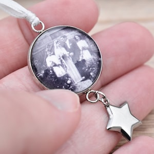 Könnte beinhalten: Ein silberner Anhänger mit einem Schwarzweißfoto einer Hochzeitszeremonie in einem runden Glascabochon. Ein silberner Sternanhänger hängt am unteren Ende des Anhängers.