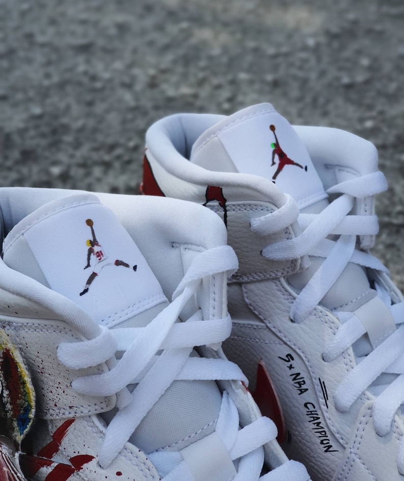 May include: White leather high-top sneakers with red and white paint splatters. The sneakers feature a white leather tongue with a black and red silhouette of a basketball player. The right shoe has the text "5 x NBA Champion" written on the side.