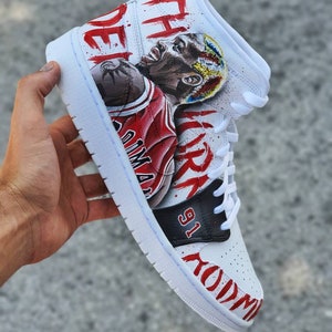 May include: White high-top sneakers with a custom hand-painted design featuring a basketball player in a red and black jersey with the text "The Air Jordan" and "91" on the side.