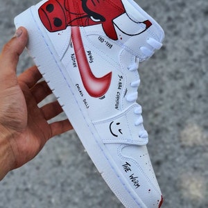 May include: White high-top sneakers with a red and black cartoon bull on the side. The text "Dennis Rodman" and "Chicago Bulls" are written on the side of the shoe. The text "5x NBA Champion" and "1995-1998" are also written on the side of the shoe. The text "The Worm" is written on the bottom of the shoe.
