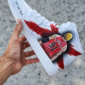 May include: White high-top sneakers with red and black paint splatters. The sneakers feature a basketball player with the number 91 and the name "Rodman" on the side. The text "Play Your Role" is written on the side of the shoe.