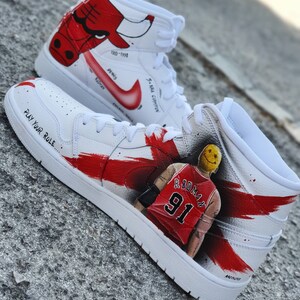 May include: White high-top sneakers with red and black accents. The sneakers feature a painted image of a basketball player with the number 91 on his jersey. The text "PLAY YOUR RULE" is written on the side of the shoe.