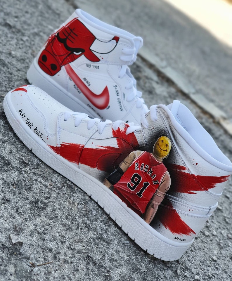 May include: White high-top sneakers with red and black accents. The sneakers feature a painted image of a basketball player with the number 91 on his jersey. The text "PLAY YOUR RULE" is written on the side of the shoe.