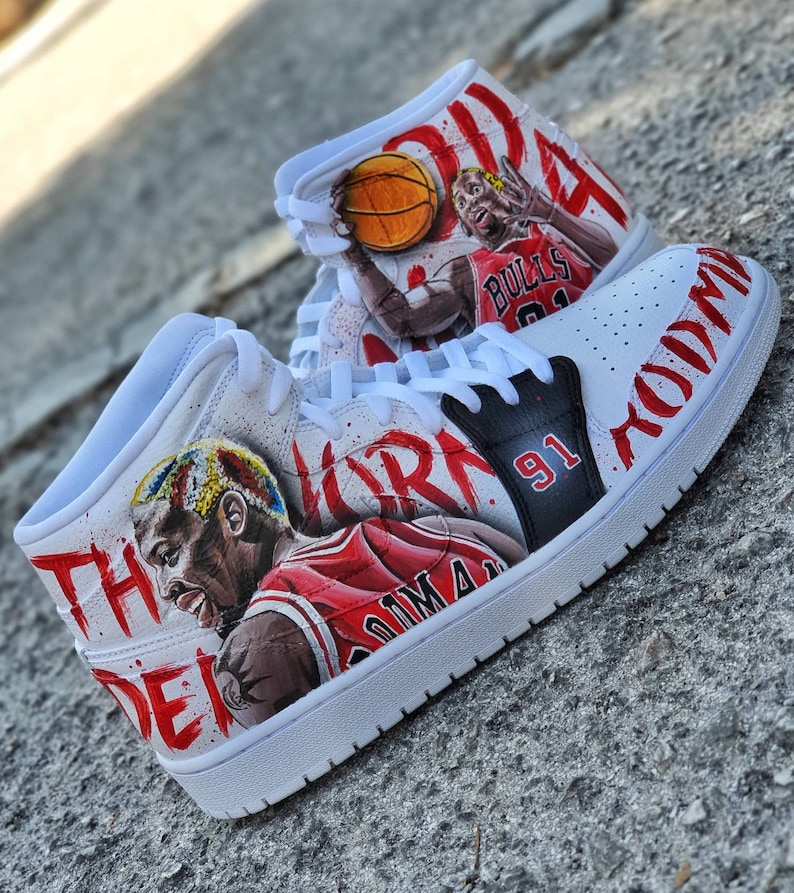 May include: White high-top sneakers with a red and black design featuring a basketball player with the number 91 on the side. The text "The" and "Jordan" are written on the shoe.
