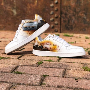 May include: A pair of white trainers with a custom design featuring a razor blade and the text "By order of the Peaky Blinders".