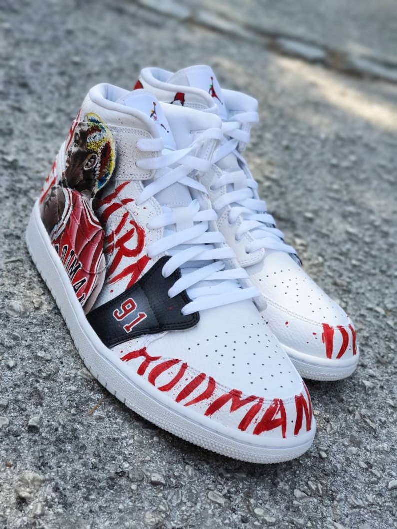 May include: White leather high-top sneakers with red and black paint detailing. The sneakers feature a basketball player graphic and the text "91" and "Jordan" on the side.