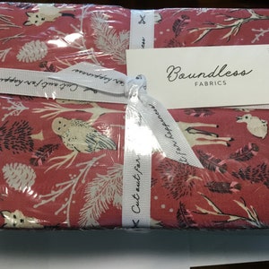 Puede incluir: Un paquete de tela envuelto en plástico transparente, con un fondo rojo y un patrón de bosque blanco de zorros, búhos y piñas. Una cinta blanca con el texto "Cut out for happiness" está atada alrededor del paquete. Una etiqueta dice "Boundless FABRICS".