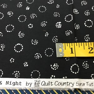 May include: Black fabric with a white dotted circle pattern. A yellow measuring tape shows the fabric's width. The fabric has the text "Day & Night by Quilt Country Sara Tuttle & Sara".