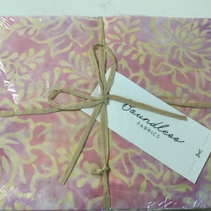 May include: A package of fabric wrapped in clear plastic and tied with a natural-colored ribbon. The fabric has a floral pattern in shades of pink and yellow. A white tag with the words "Boundless Fabrics" is attached.